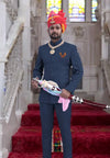Elegant man in Eagle Logo Jodhpuri Suit with traditional turban, holding a ceremonial sword in a royal setting