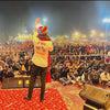 Man wearing Om Banna logo shirt by Modern Marwar addressing large outdoor crowd at night event