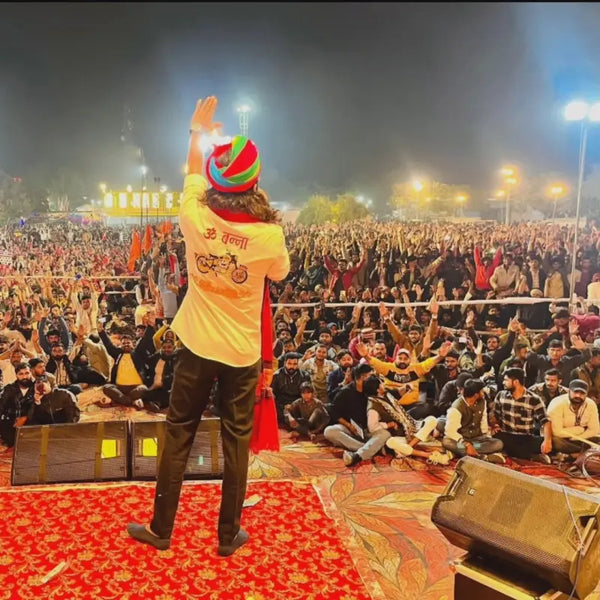 Man wearing Om Banna logo shirt by Modern Marwar addressing large outdoor crowd at night event