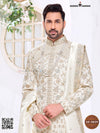 Elegant traditional Indian groom outfit in cream with intricate embroidery and a stylish shawl